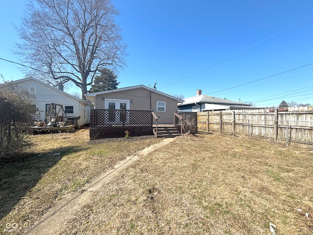 rear view of house with a wooden deck, a lawn, french doors, and fence