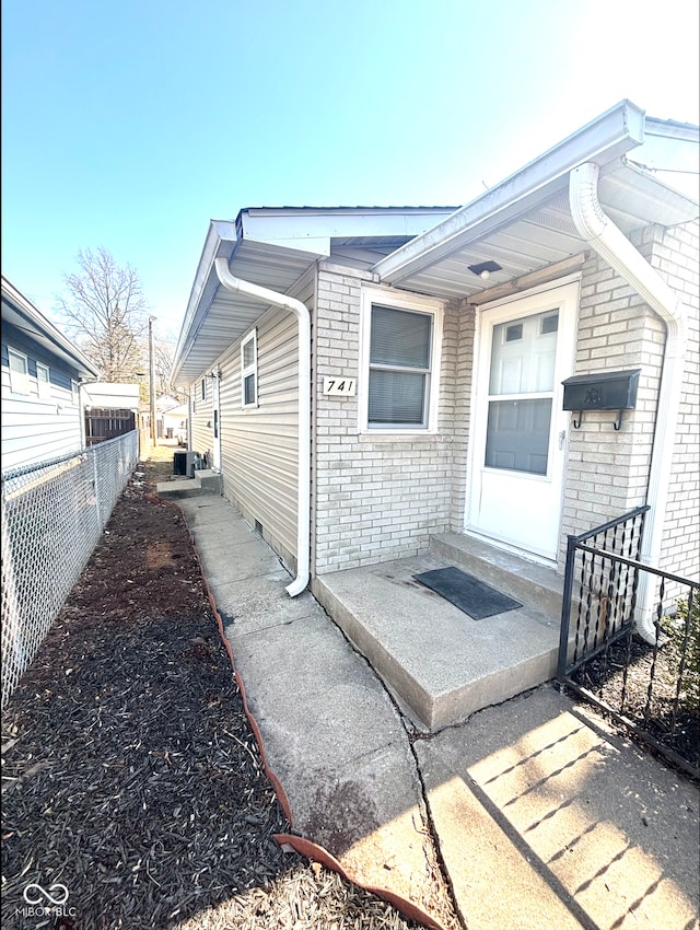 view of exterior entry with brick siding and fence