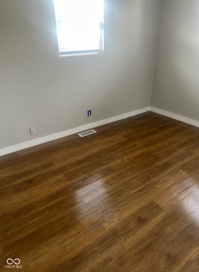 empty room featuring visible vents, dark wood-type flooring, and baseboards