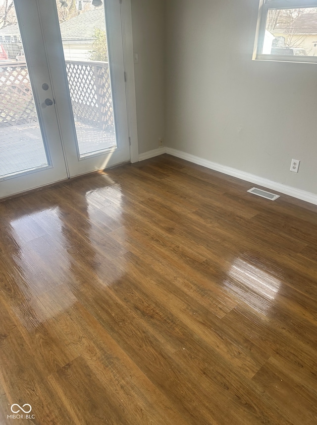 unfurnished room with dark wood-style flooring, baseboards, visible vents, and a wealth of natural light