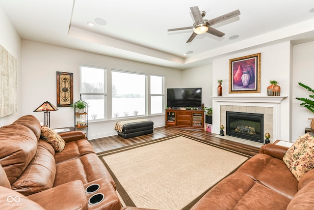 living room with a fireplace, a raised ceiling, ceiling fan, and wood-type flooring