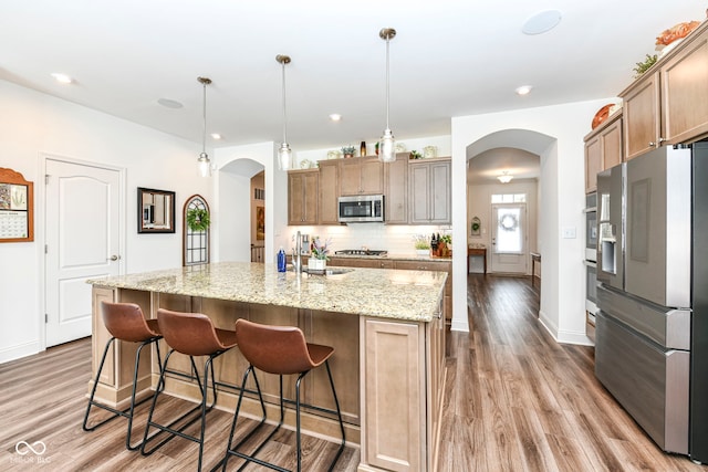 kitchen with stainless steel appliances, sink, backsplash, hanging light fixtures, and a center island with sink