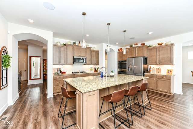 kitchen with appliances with stainless steel finishes, an island with sink, pendant lighting, a kitchen bar, and decorative backsplash