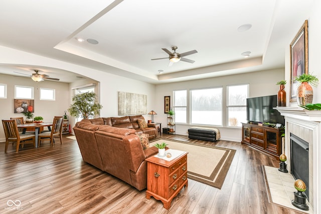 living room featuring wood-type flooring, ceiling fan, and a tray ceiling