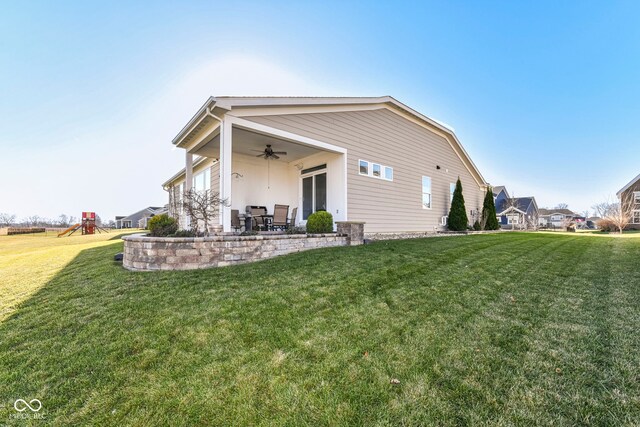 rear view of property with ceiling fan, a playground, and a lawn