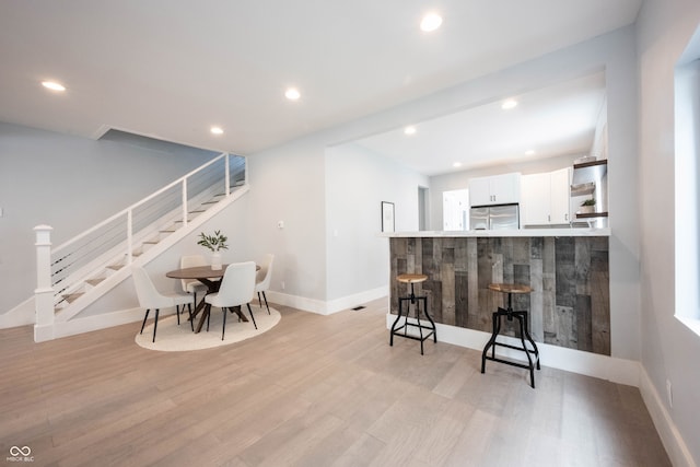 bar with stainless steel refrigerator, white cabinets, and light hardwood / wood-style floors