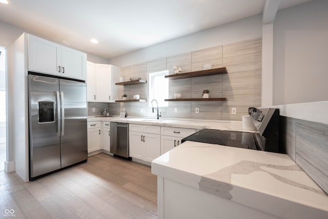 kitchen featuring sink, light stone counters, appliances with stainless steel finishes, white cabinets, and light wood-type flooring