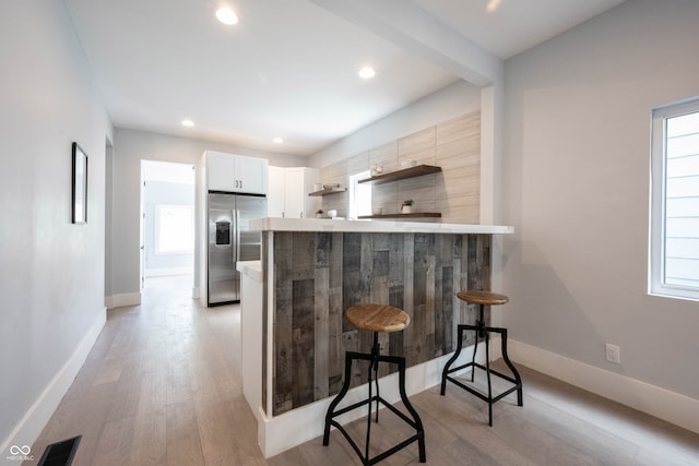 kitchen featuring kitchen peninsula, light hardwood / wood-style flooring, white cabinets, stainless steel fridge with ice dispenser, and a breakfast bar area