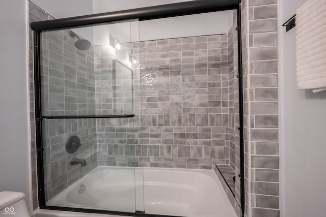 bathroom featuring toilet and shower / bath combination with glass door