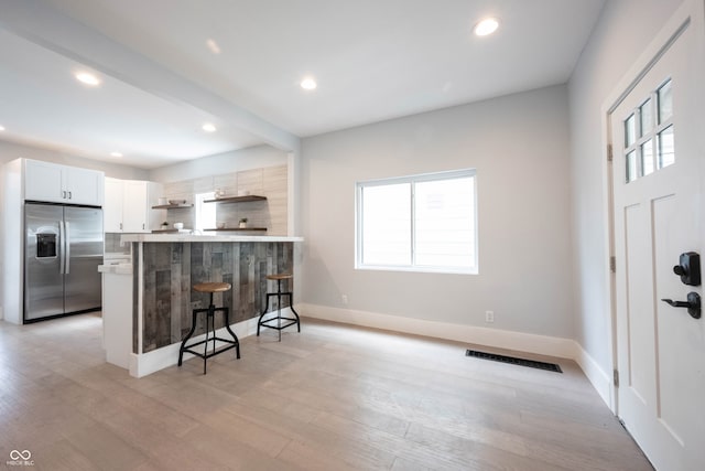 kitchen featuring stainless steel refrigerator with ice dispenser, kitchen peninsula, a kitchen bar, white cabinets, and light wood-type flooring