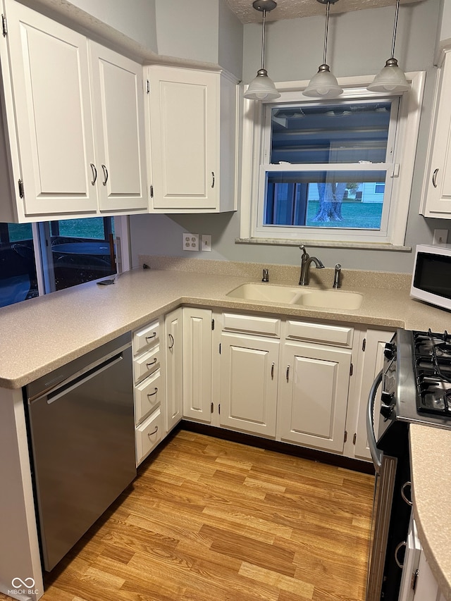 kitchen featuring sink, hanging light fixtures, stainless steel dishwasher, white cabinets, and light wood-type flooring