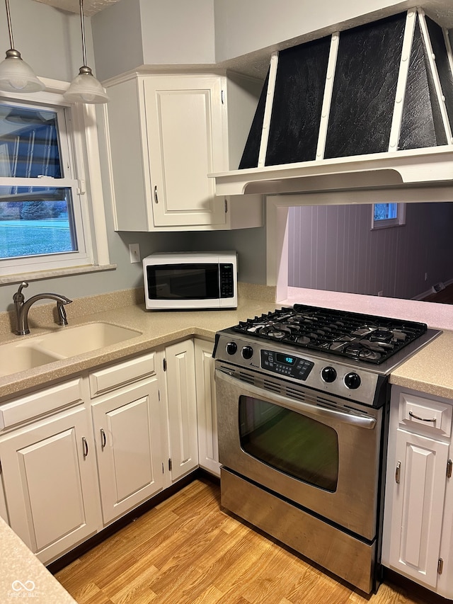 kitchen with white cabinetry, sink, hanging light fixtures, stainless steel gas range oven, and light wood-type flooring