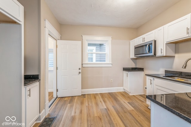 kitchen with a textured ceiling, sink, light hardwood / wood-style flooring, dark stone countertops, and white cabinetry