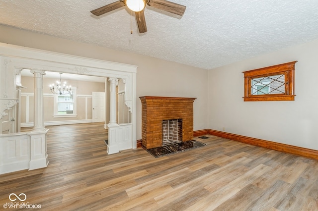 unfurnished living room featuring decorative columns, a textured ceiling, ceiling fan with notable chandelier, a fireplace, and hardwood / wood-style floors