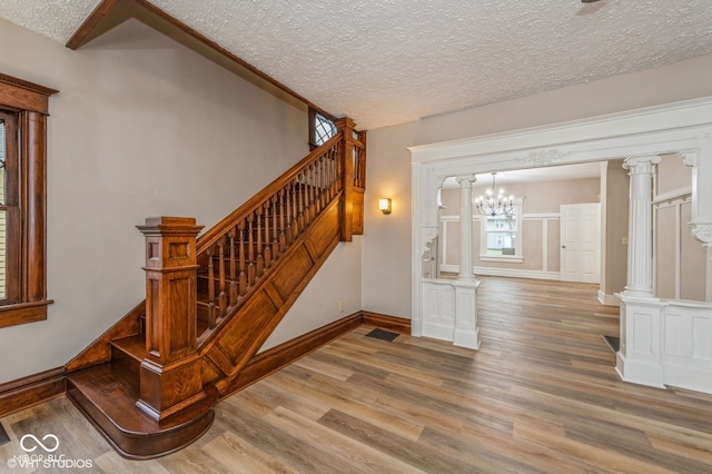 stairway with decorative columns, hardwood / wood-style floors, a chandelier, and a textured ceiling