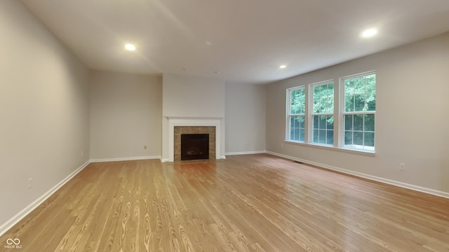 unfurnished living room featuring light hardwood / wood-style floors and a tiled fireplace