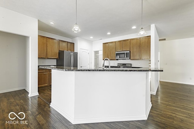 kitchen with stainless steel appliances, a center island with sink, decorative light fixtures, and dark stone counters