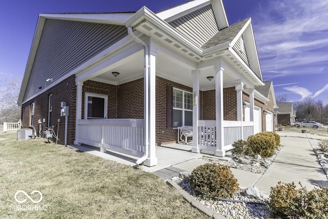 view of side of home featuring a garage, covered porch, a lawn, and brick siding