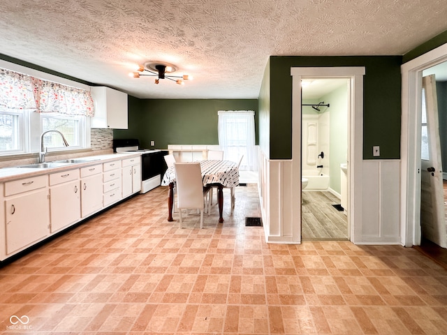 kitchen featuring sink, tasteful backsplash, white range with electric cooktop, a textured ceiling, and white cabinets