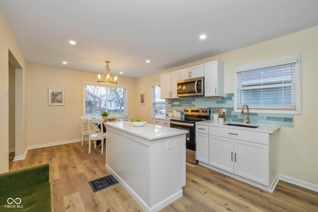 kitchen featuring white cabinetry, sink, decorative light fixtures, appliances with stainless steel finishes, and light wood-type flooring