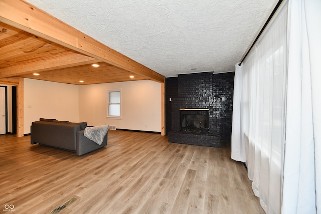 living room with beamed ceiling, light hardwood / wood-style floors, a textured ceiling, and a brick fireplace