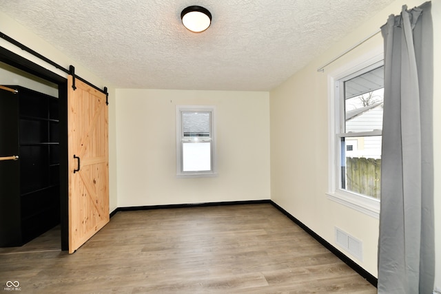 empty room featuring a barn door, light wood-type flooring, and a textured ceiling