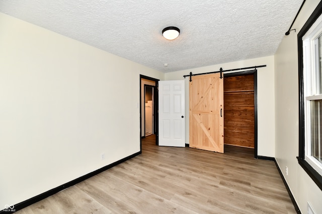 unfurnished bedroom featuring light wood-type flooring, a textured ceiling, a barn door, and a closet