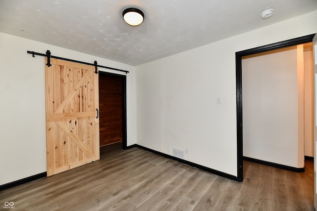 unfurnished bedroom with a barn door and hardwood / wood-style flooring