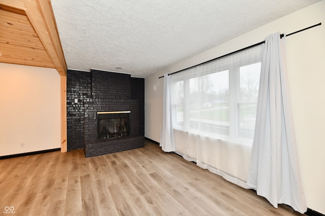 unfurnished living room featuring light hardwood / wood-style flooring, beamed ceiling, a textured ceiling, and a brick fireplace