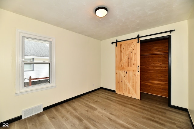 unfurnished bedroom featuring a barn door, wood-type flooring, and a closet