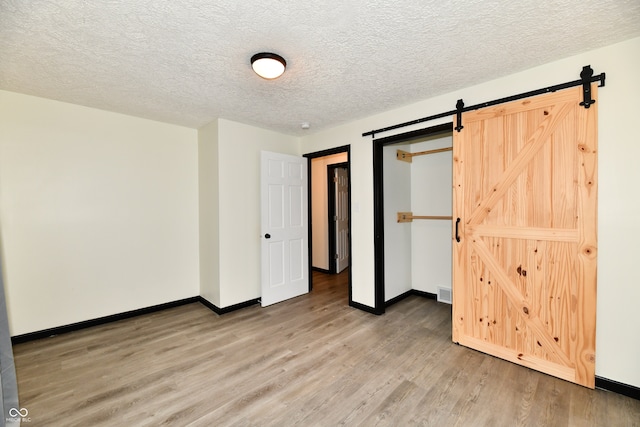 unfurnished bedroom featuring a barn door, wood-type flooring, and a textured ceiling