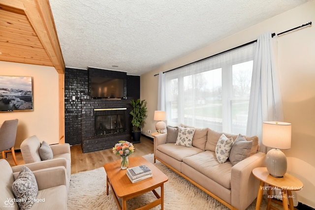 living room with beam ceiling, light hardwood / wood-style flooring, a textured ceiling, and a brick fireplace