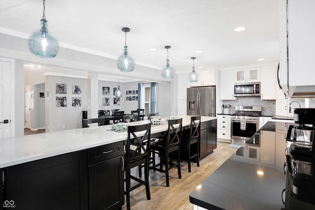 kitchen with light hardwood / wood-style floors, crown molding, hanging light fixtures, and appliances with stainless steel finishes