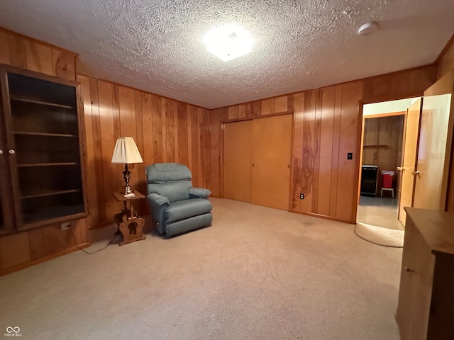 unfurnished room featuring a textured ceiling, light colored carpet, and wooden walls