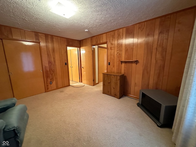 interior space featuring a textured ceiling, light colored carpet, and wooden walls