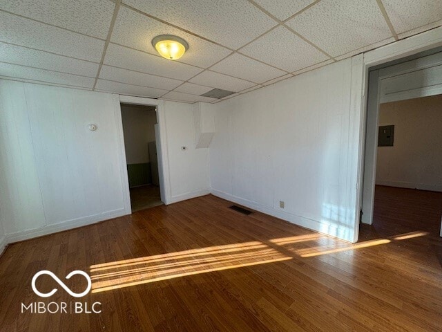 spare room with a paneled ceiling, wood-type flooring, and electric panel