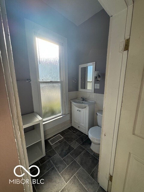 bathroom featuring vanity, toilet, and tile walls