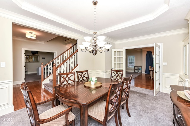 dining space featuring french doors, ornamental molding, a tray ceiling, a notable chandelier, and hardwood / wood-style floors