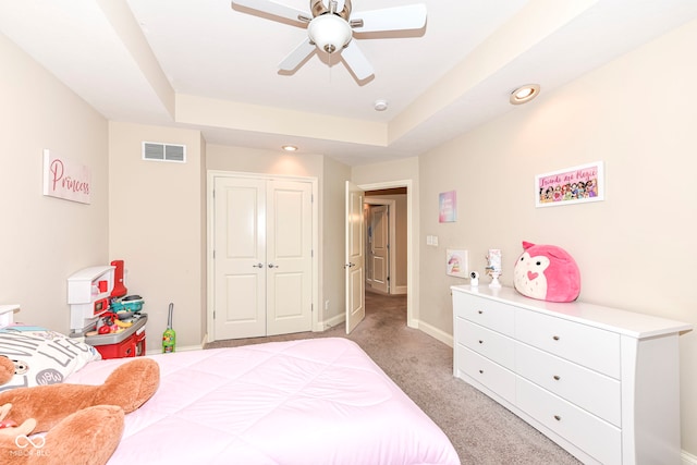 carpeted bedroom featuring ceiling fan, a raised ceiling, and a closet