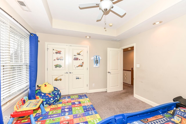 carpeted bedroom featuring a closet, ceiling fan, and a tray ceiling