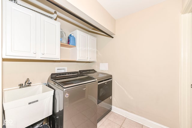 laundry area featuring separate washer and dryer, sink, light tile patterned floors, and cabinets