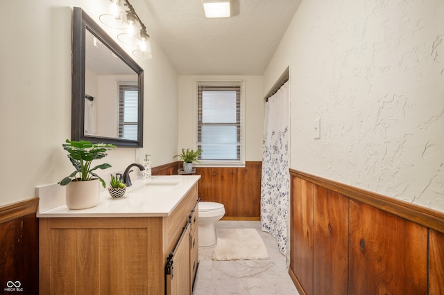 bathroom featuring a textured ceiling, vanity, toilet, and wood walls