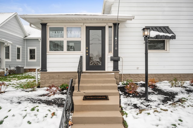 snow covered property entrance featuring central AC unit