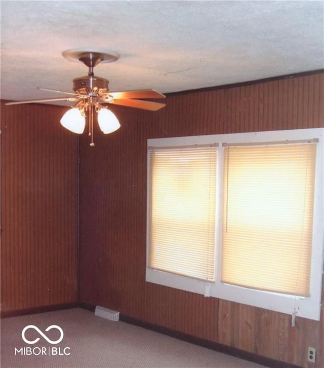 spare room featuring carpet flooring, a textured ceiling, ceiling fan, and wood walls