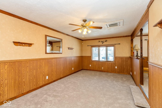 carpeted empty room featuring crown molding, ceiling fan, wooden walls, and a textured ceiling