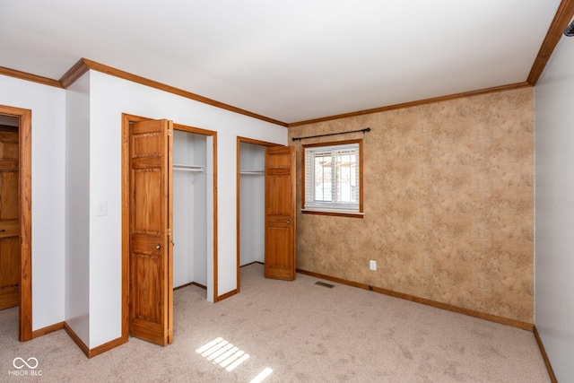 unfurnished bedroom with crown molding, light carpet, and two closets