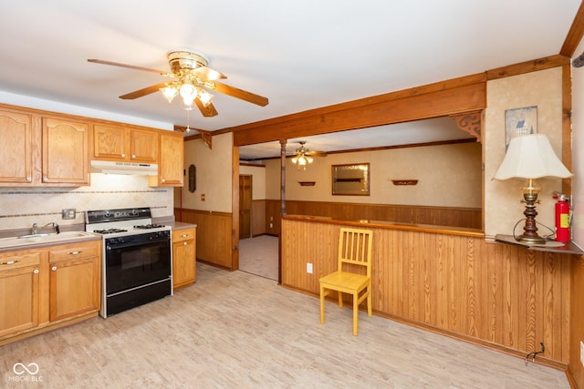 kitchen with sink, range with gas cooktop, light wood-type flooring, wooden walls, and ceiling fan