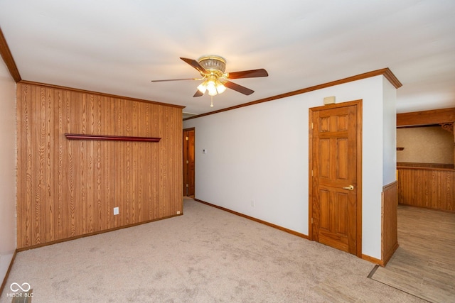 carpeted spare room with crown molding, wooden walls, and ceiling fan