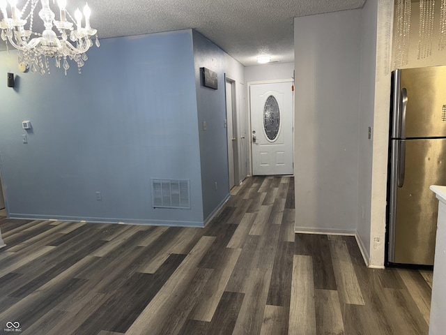 corridor with a textured ceiling, dark wood-type flooring, and a chandelier