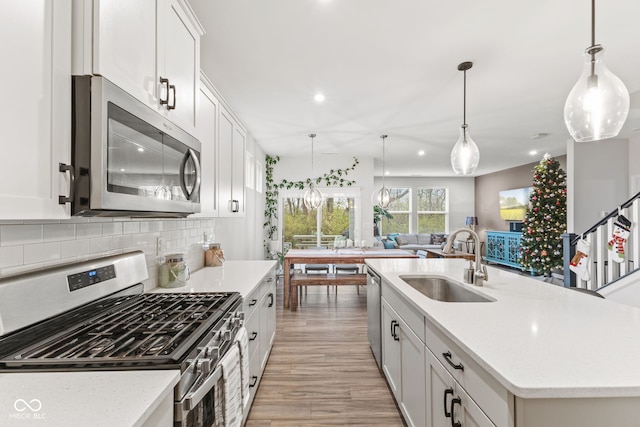 kitchen with stainless steel appliances, sink, a center island with sink, light hardwood / wood-style flooring, and white cabinets